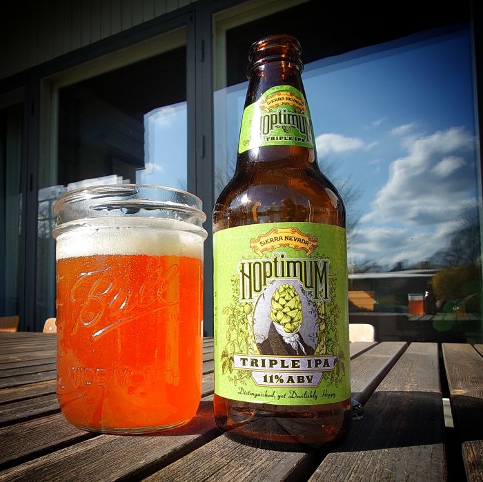 En flaska och ett glas öl på ett bord utomhus i solskenet.