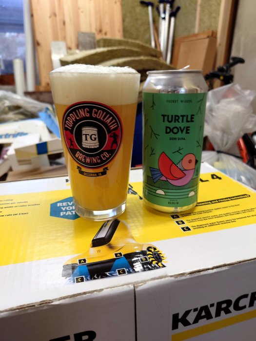 Ett ölglas med skum, en burk Turtle Dove DIPA, verktygarbetsplats i bakgrunden, på en Kärcher låda.