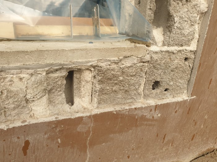 Närbild på en cementblockvägg med isolering ovanpå, delvis oskyddad, i konstruktionsområde.