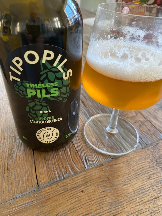 Ölflaska märkt "TIPOPILS", ölglas med skum, träbord, Bryggeri italienska, "Timeless Pils".