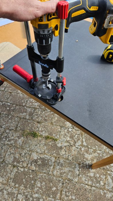 Gul borrmaskin monterad på ställning för precision, på svart bord mot stenmark.