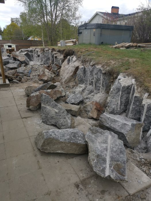 Byggarbetsplats med sprängda stenar, grova block, grusväg, och arbetsmaterial i bakgrunden.