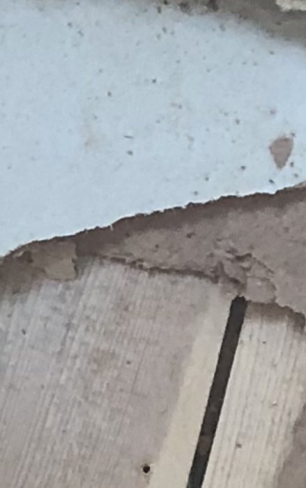 Närbild på slitna material: skadad spånskiva, vit yta ovan, oskarp bakgrund.
