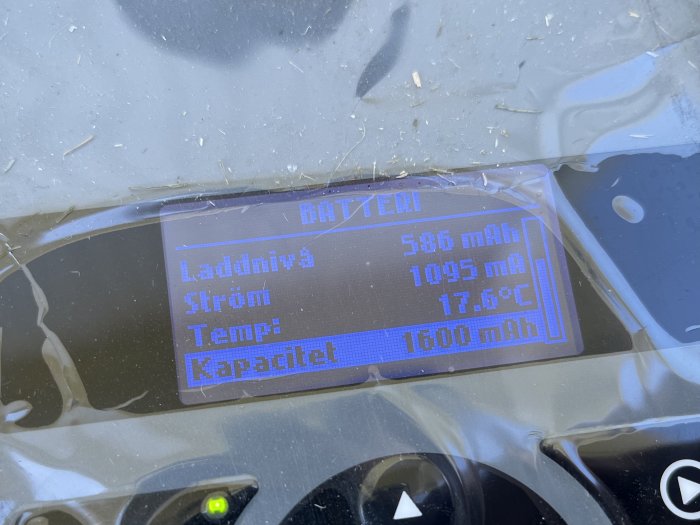 Digital display visar batteriinformation: laddning, ström, temperatur och kapacitet. Verkar inramad av plast.