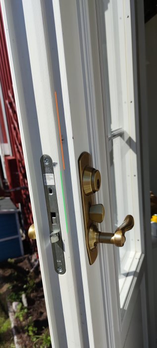 Vitt fönster öppnat utåt; gyllene handtag och lås; soligt, med skuggor; grönt gräs syns ute.
