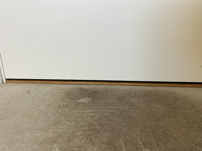 Vägg möter golv; grått betonggolv, vit vägg, trälist, skavanker, minimalism.