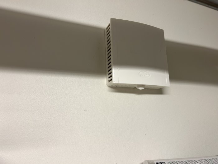 Vit ventilationsenhet på vägg med skuggor, märkt med "Fresh", minimalistisk inomhusmiljö.