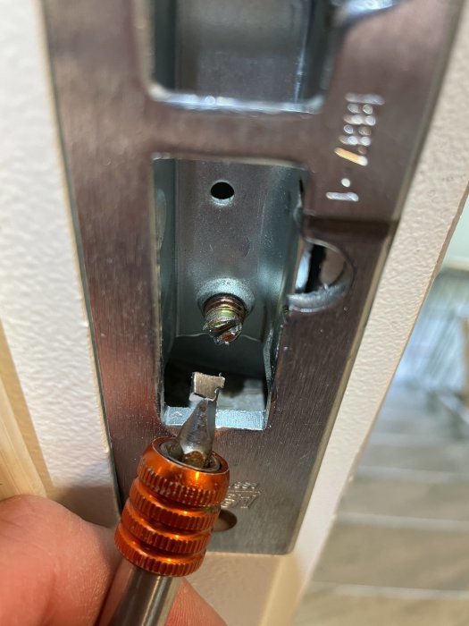 Skruvmejsel demonterar eller monterar lås i dörr, hemmaförbättring, närbild, fokus på metallmekanism, manuellt arbete.