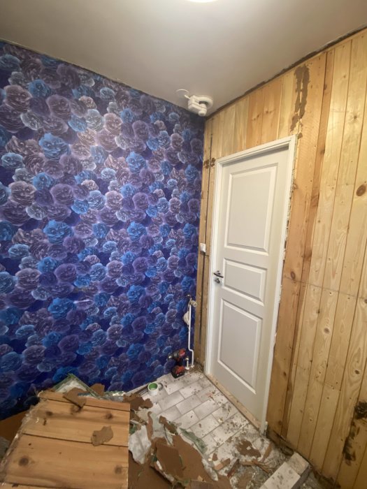 Ett rum under renovering, blommig tapet, trälådor, verktyg och byggavfall på golvet.