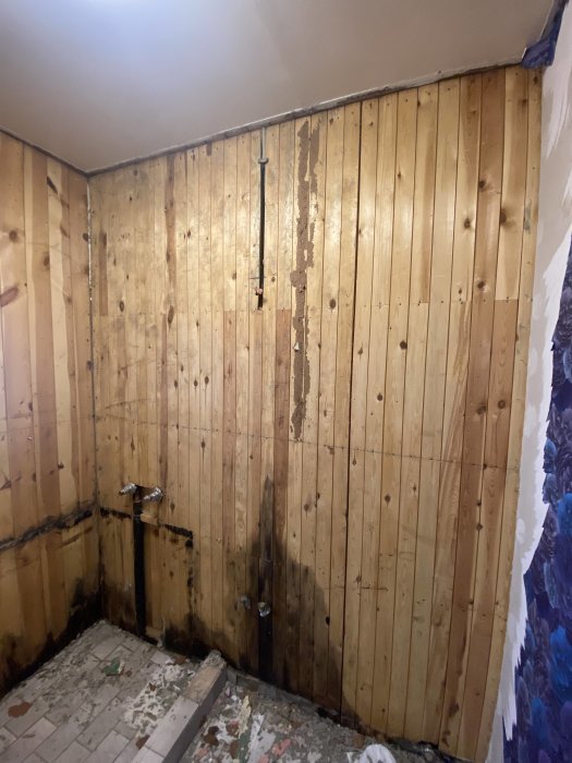 Renoveringsprojekt, träpanelväggar, vattenskador, avskalad tapet, rörinstallationer synliga, golv i oordning.
