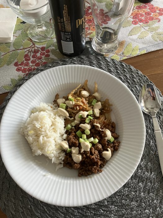 Tallrik med ris, köttfärs, böngroddar, gröna lökar och vit sås på ett bord.