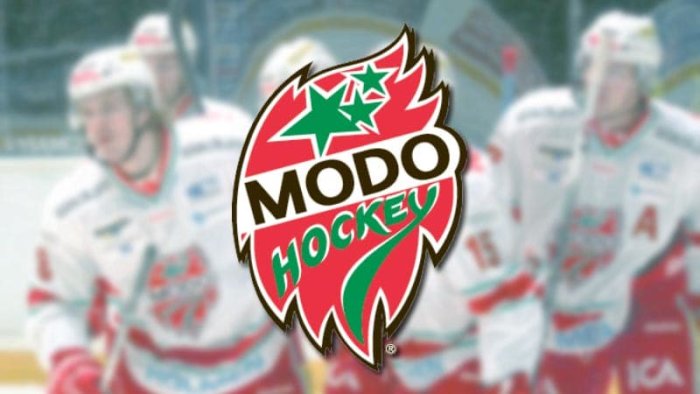 Ishockeyspelare i suddig bakgrund med "MODO Hockey"-logotypen i fokus, röd-grön med text, svensk klubbrepresentation.