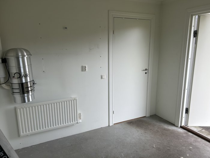 Tomt rum med vädringsanordning, radiator, dörr, spår av borttagna föremål på vägg, oinredd golv.