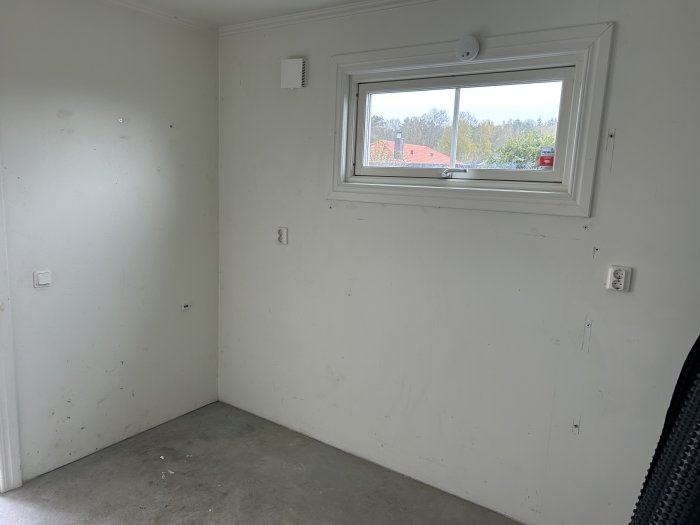 Tomt rum med vita väggar, fönster, synlig smuts och betonggolv.