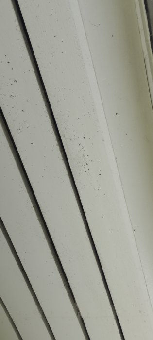 Vit panelvägg med vertikala lister, smutsfläckar och kabel eller spricka i fog.