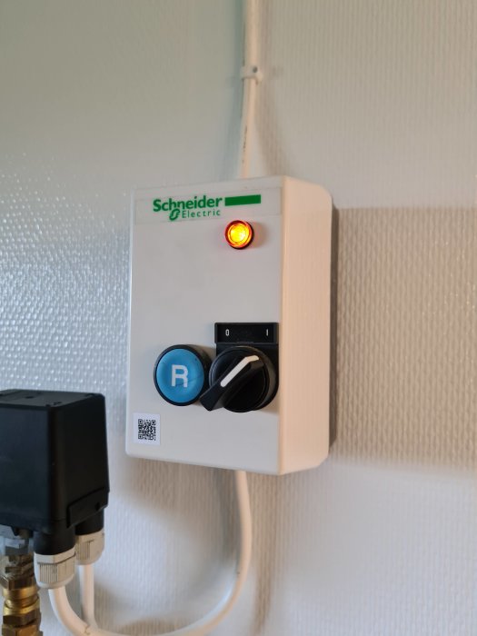 En väggmonterad Schneider Electric-enhet med grönt märke, röd lysdiod, vred och QR-kod.