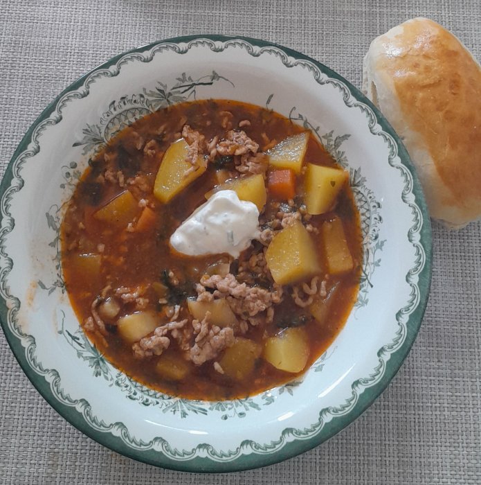 Gryta med köttfärs, potatis, en klick gräddfil på tallrik, bit bröd vid sidan.