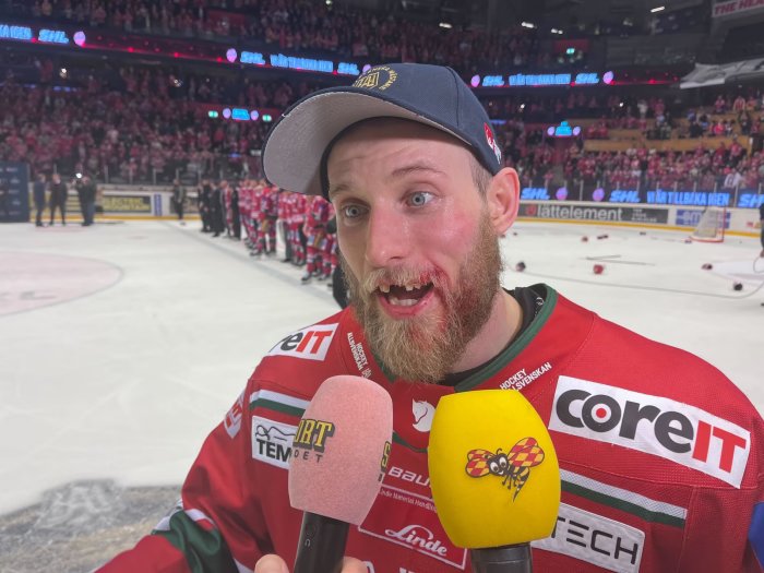 Ishockeyspelare intervjuas, blodig, glädje, publik och lagkamrater i bakgrunden, röd tröja, firande.