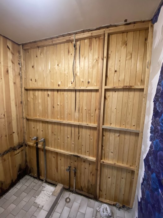 Orenoverat rum med träpaneler, synliga rör, kala golv och väggar i ombyggnadsfas.