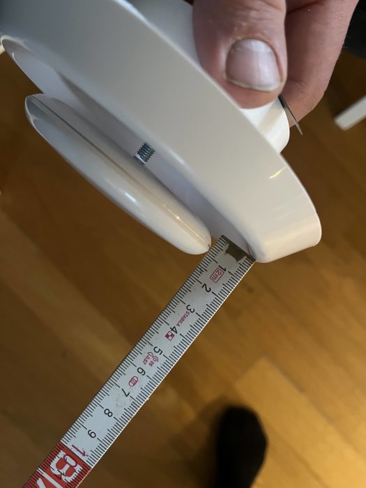 En hand håller ett vitt föremål över ett måttband som visar cirka 9 centimeter.