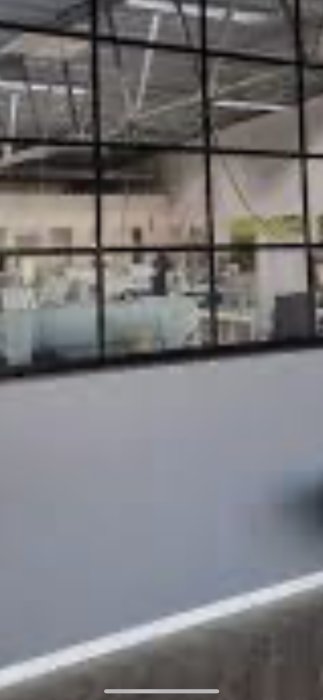 Oskarp bild, stor byggnad ses genom svarta fönsterramar, modern arkitektur, reflektioner, möjlig kontorsmiljö inomhus.