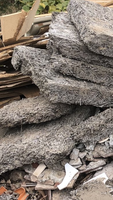 Högar av asbestplattor blandat med skräp och bråte på en rivningsplats. Farligt om inte hanteras korrekt.