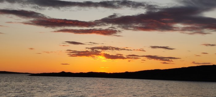 Solnedgång över havet med moln och varma färger på himlen.