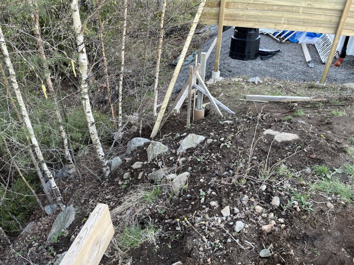Skogsdunge, stenar, jord, virke, byggmaterial, konstruktion, svart behållare, utomhus, oordnad, vårdag.