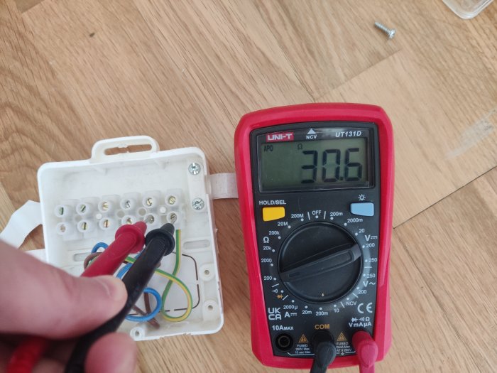 Mätning av elektrisk spänning med en multimeter; kablar, kontaktuttag på träyta.