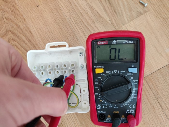 Multimeter används för att testa anslutningar i öppen elektrisk dosa; inga spänningar indikeras.