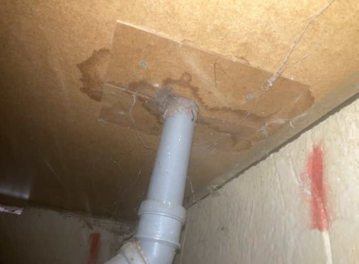 Vit rörledning, vattenskada på brun yta, genomskinligt tejp, spindelnät, möjlig mögelbildning.
