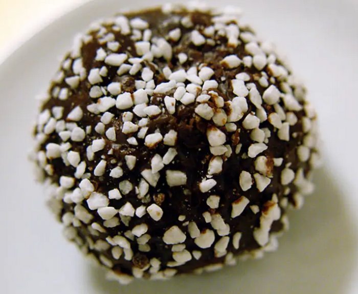 Chokladboll täckt med pärlsocker på en vit yta. Sötsak från Sverige. Snack eller fika komponent.