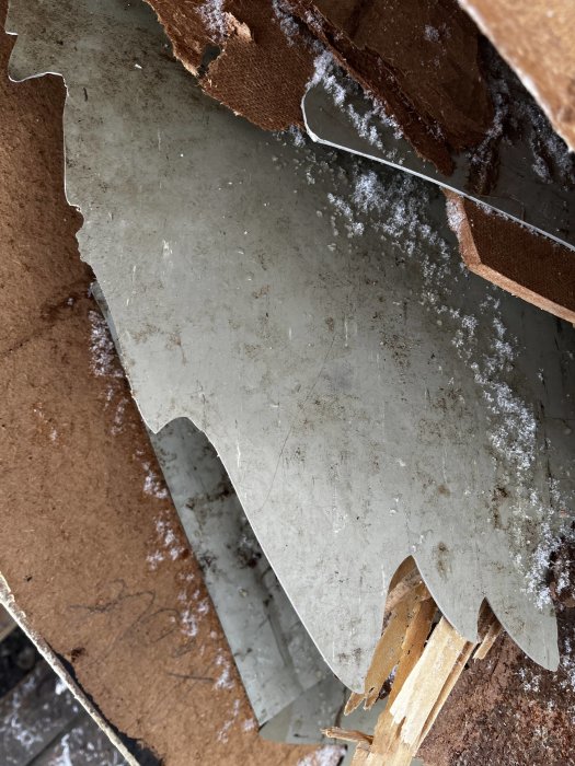 Snedvinkelbild av spruckna, överlappande material med snöflingor och rostiga ytor.