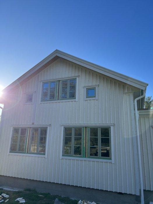 Tvåvånings trähus, vita fasader, flera fönster, solnedgång, blå himmel, byggmaterial på marken.