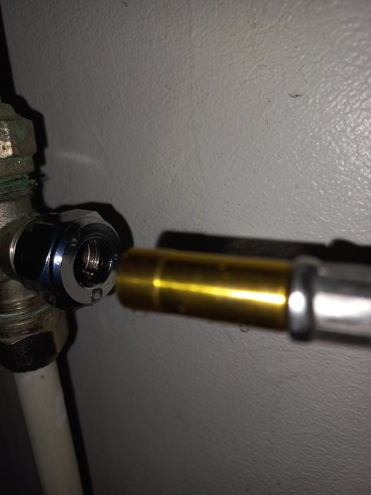 Ett rör eller en kabelanslutning med en mutter, mot en vitmålad vägg, närbild.