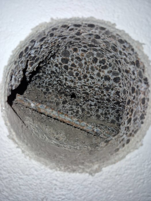 Ett sirkulärt hål i en betongvägg med synliga små stenar och en armeringsjärn.