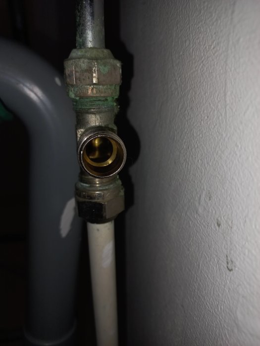 Metall vattenrörskoppling med tecken på korrosion utanför en grå vägg.