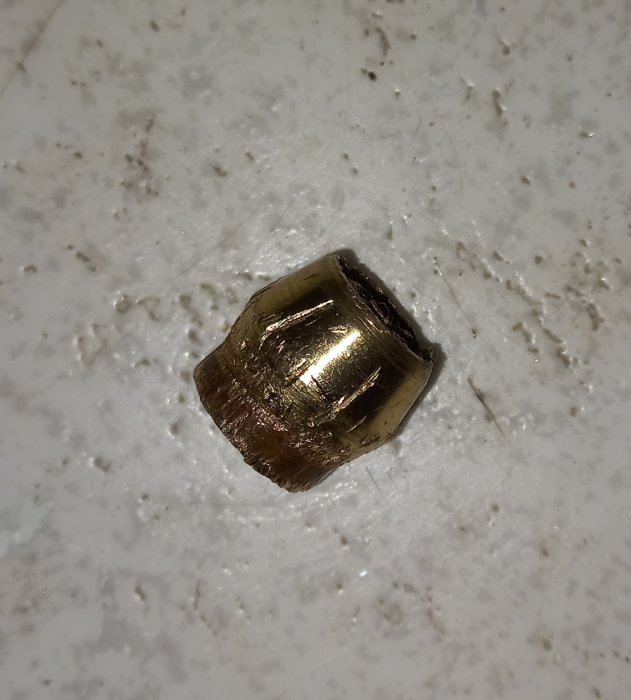 Guldfärgad mutter på en smutsig vit yta.