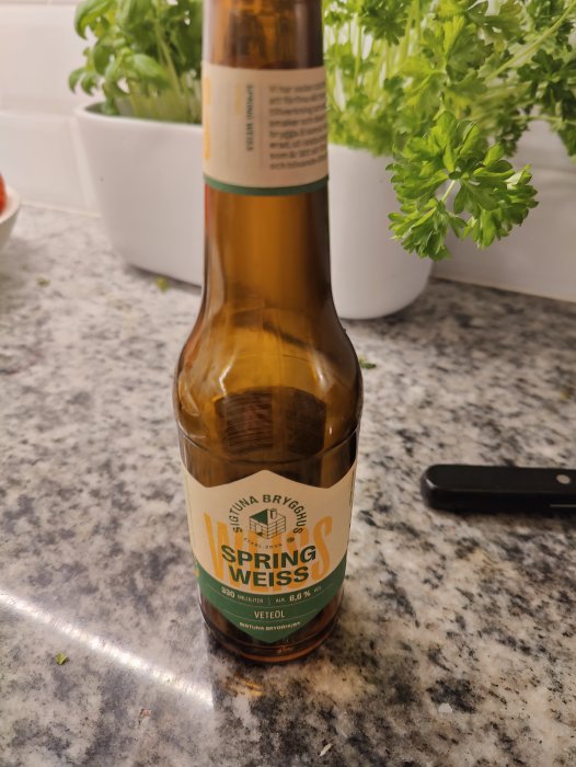 En ölflaska på ett marmorbord, märkt "Spring Weiss", bredvid gröna växter.