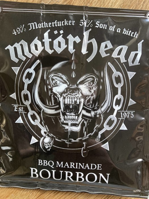 Förpackningen har en skallig illustration, varumärket "Motörhead", och texten "BBQ Marinade Bourbon". Est. 1975.