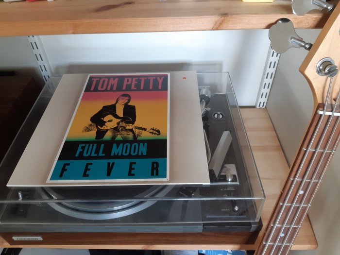 Vinylskiva av Tom Petty på skivspelare, bredvid del av basgitarr och möbler.