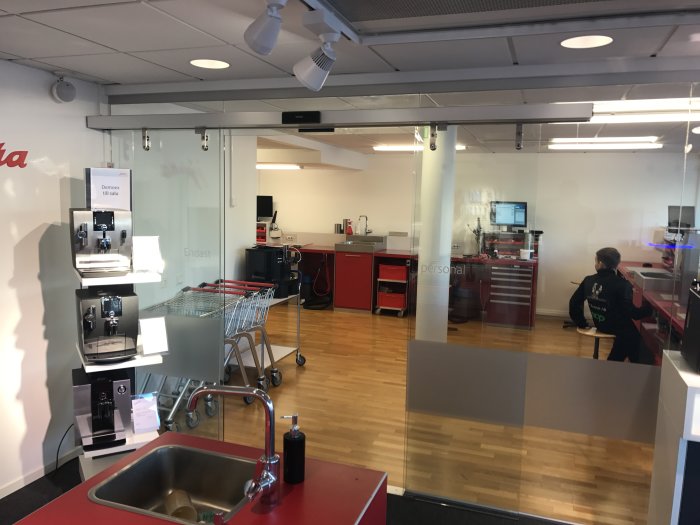 Kontorskök med kaffemaskiner, diskho, kundvagn, person och skylt som säger "Endast personal".