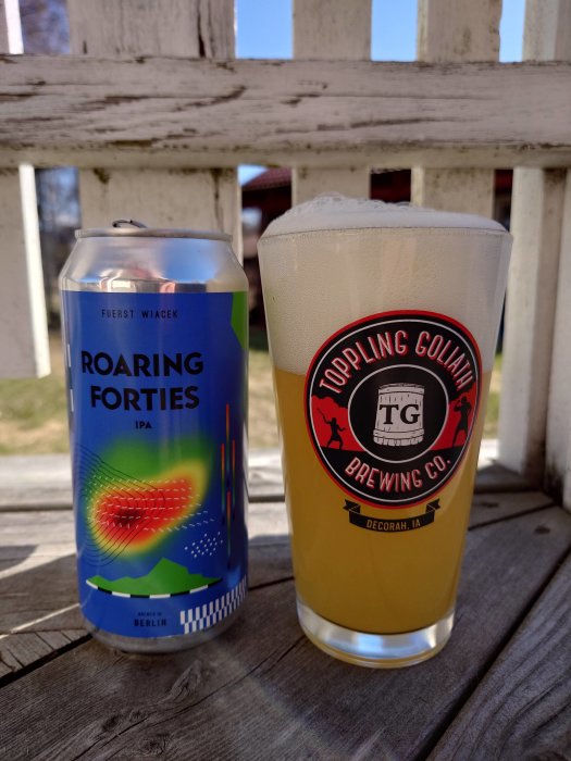 Ölburk och glas på träyta, mot vit trästaket, på en solig dag.