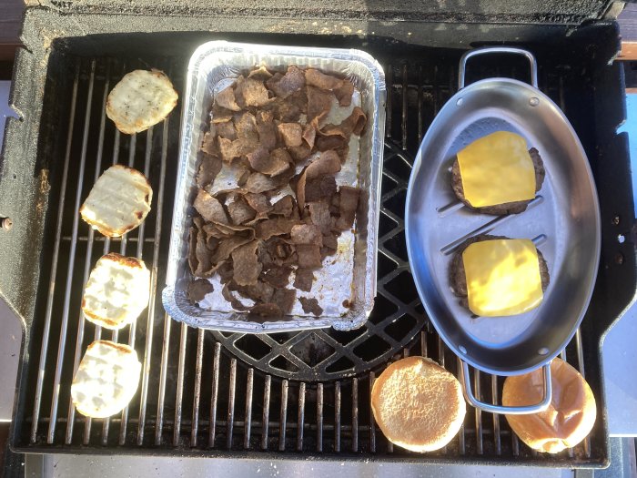 Grillning pågår: köttbitar, ostiga hamburgare, rostade brödskivor och grillad ost. Solig dag. Utomhusmatlagning.