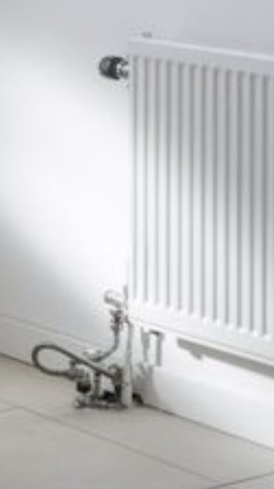 Vit radiator mot vit vägg, termostatventiler, skuggor, modern inomhus värme, minimalistisk stil.