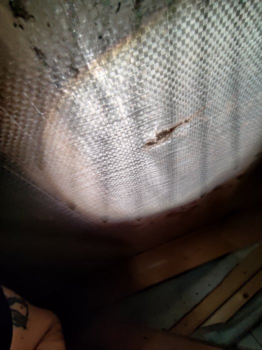 Närbild, förmodligen nött myggnät eller textil, med otydlig bakgrund och en del av en person.