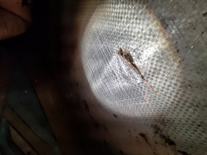 Närbild på smutsigt, skadat glasfiber eller nätstruktur, otydligt bakomfokus, ojämnt ljus, rörigt intryck.