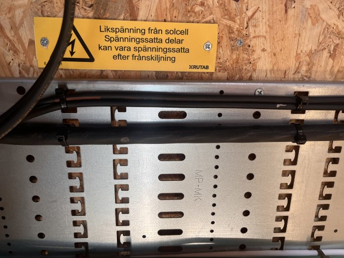 Elinstallation med varningsetikett, kablar, kabelkanal och OSB-panel i bakgrunden.