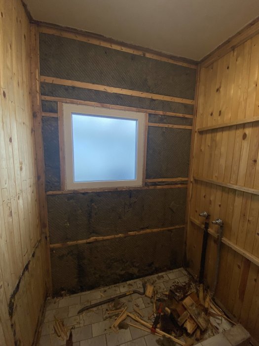 Renovering av ett rum med isolering och träpaneler som avlägsnats, fönster, skräp på golvet.