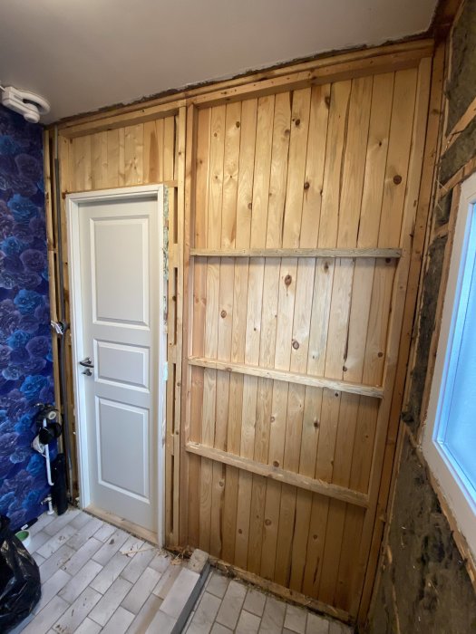 Renoveringsprojekt, träväggar, dörr, kakelgolv, kontrast tapet, exponerade reglar, inre hörn, dagljus från fönster.